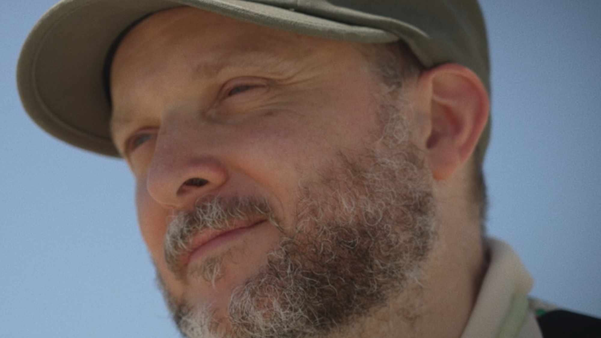 Choreograaf Sidi Larbi Cherkaoui tuurt in de verte. Hij draagt een pet en de lucht achter hem is blauw.