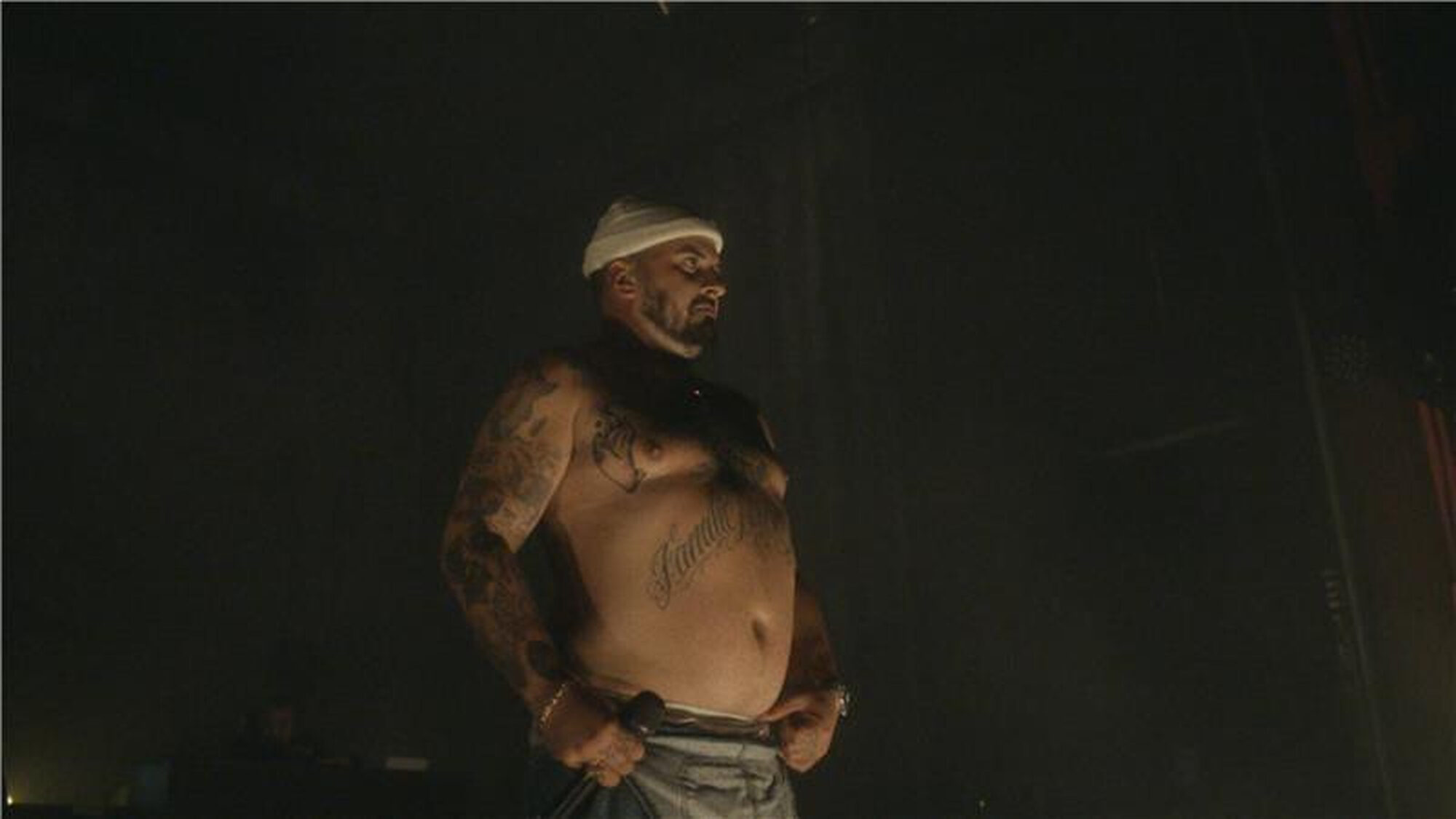 Zwangere Guy staat op een podium met een witte muts op en heeft een blote buik