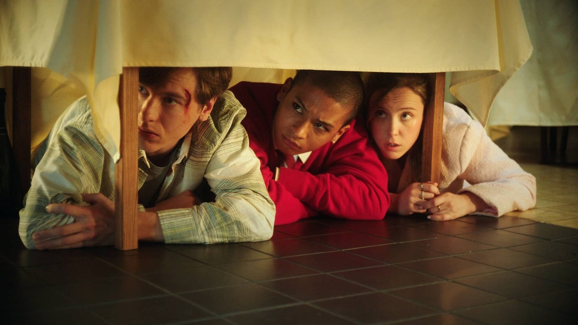 Drie jonge mensen liggen onder een tafel tijdens een gijzeling in een restaurant