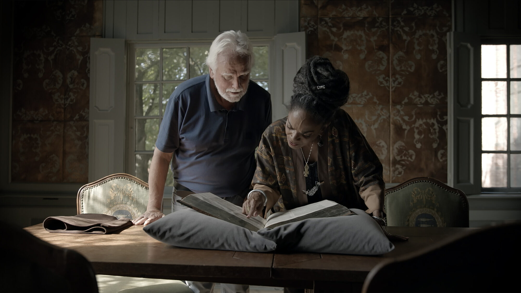 Presentatrice Aldith Hunkar en een man kijken samen met een oudere man in een historisch boek.