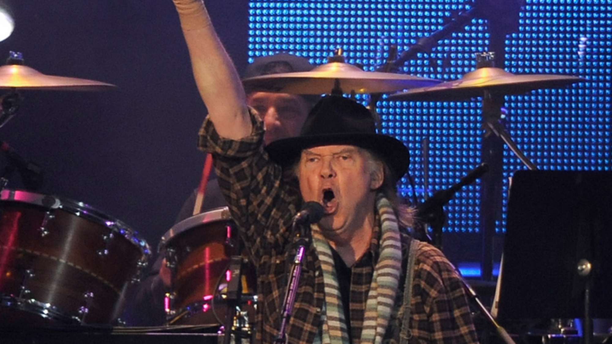 Neil Young treedt op en steekt zijn vuist in de lucht tijdens het zingen.