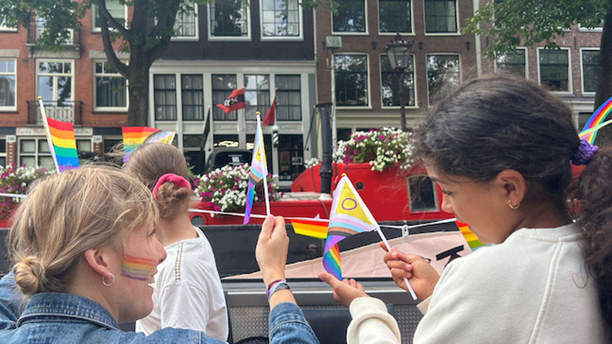 Een meisje en een mevrouw van Theater De Krakeling zwaaien met vlaggetjes naar de voorbijgangers vanaf de boot in Amsterdam.