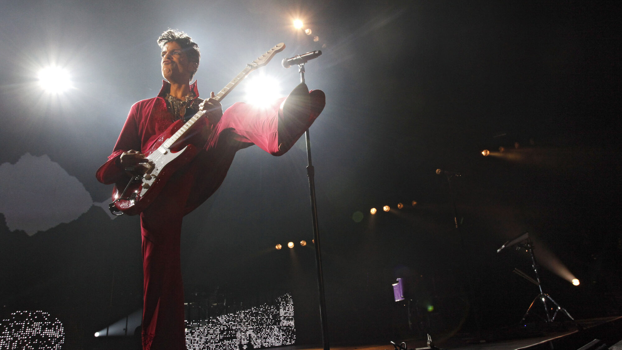 Persoon in een rood pak met een rode gitaar staat te spelen op een podium