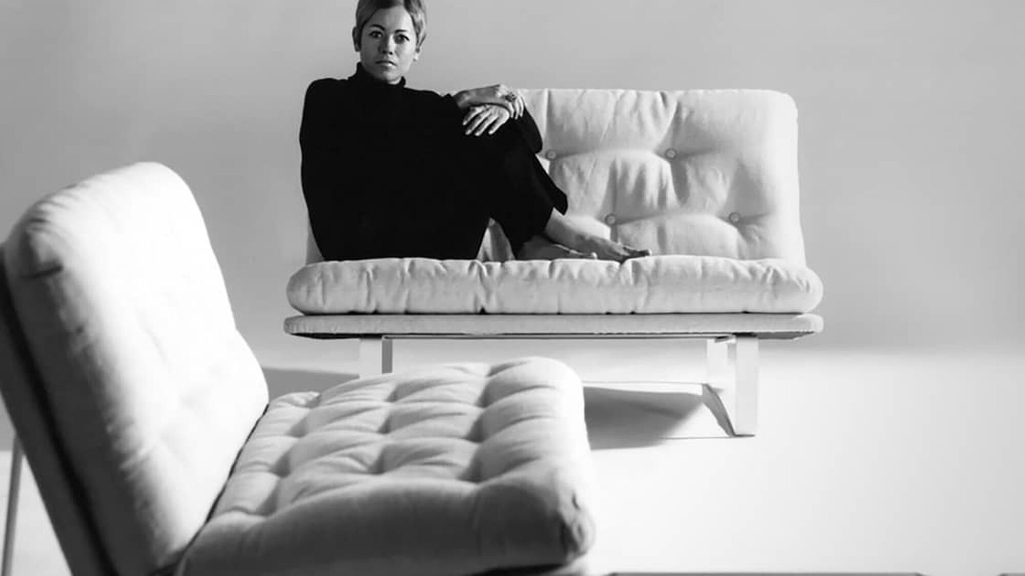 Zwart witte foto met vrouw in de hoek van een designer bank kijkend naar de camera