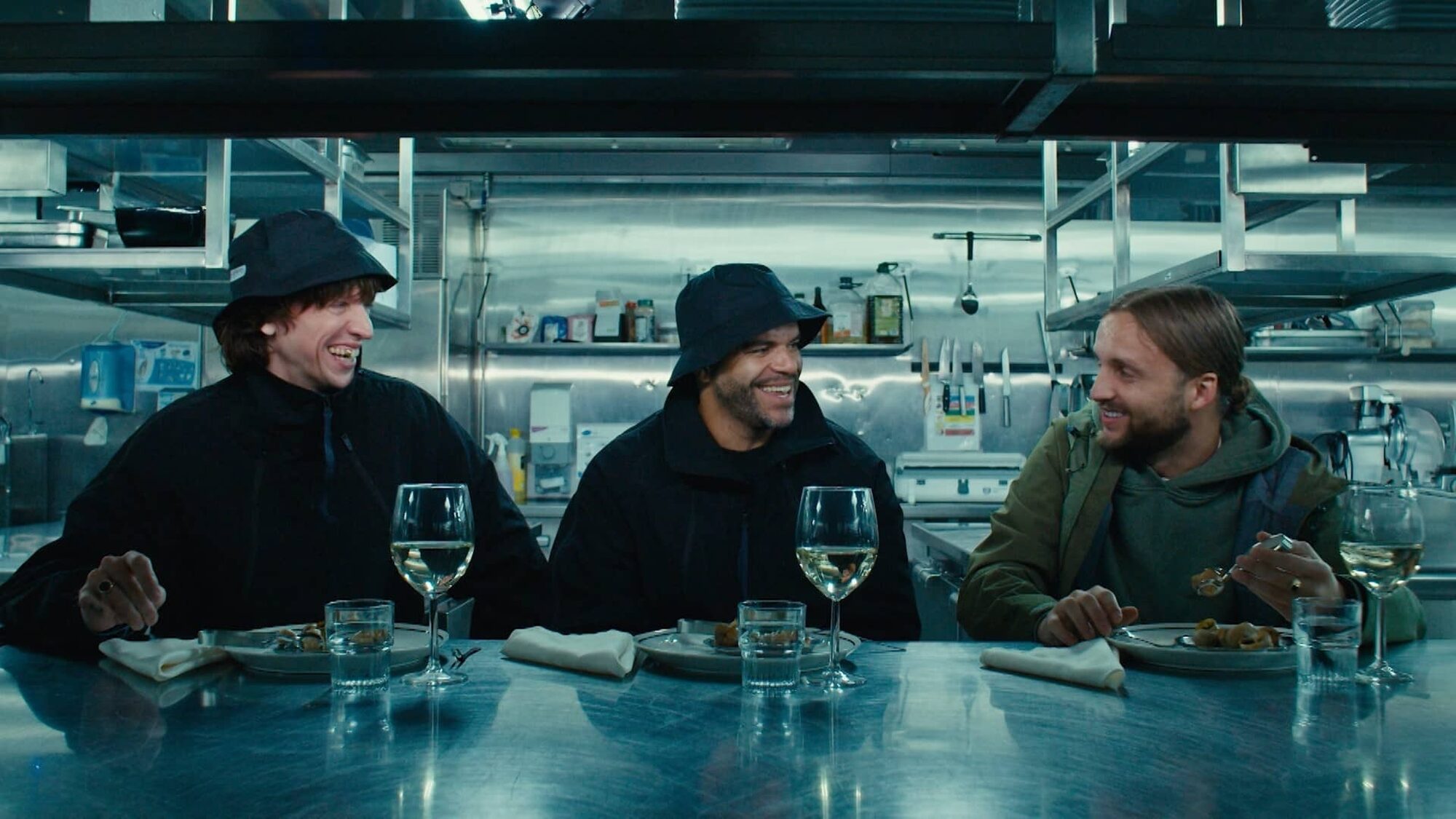 Drie personages uit de serie zitten met elkaar aan tafel.