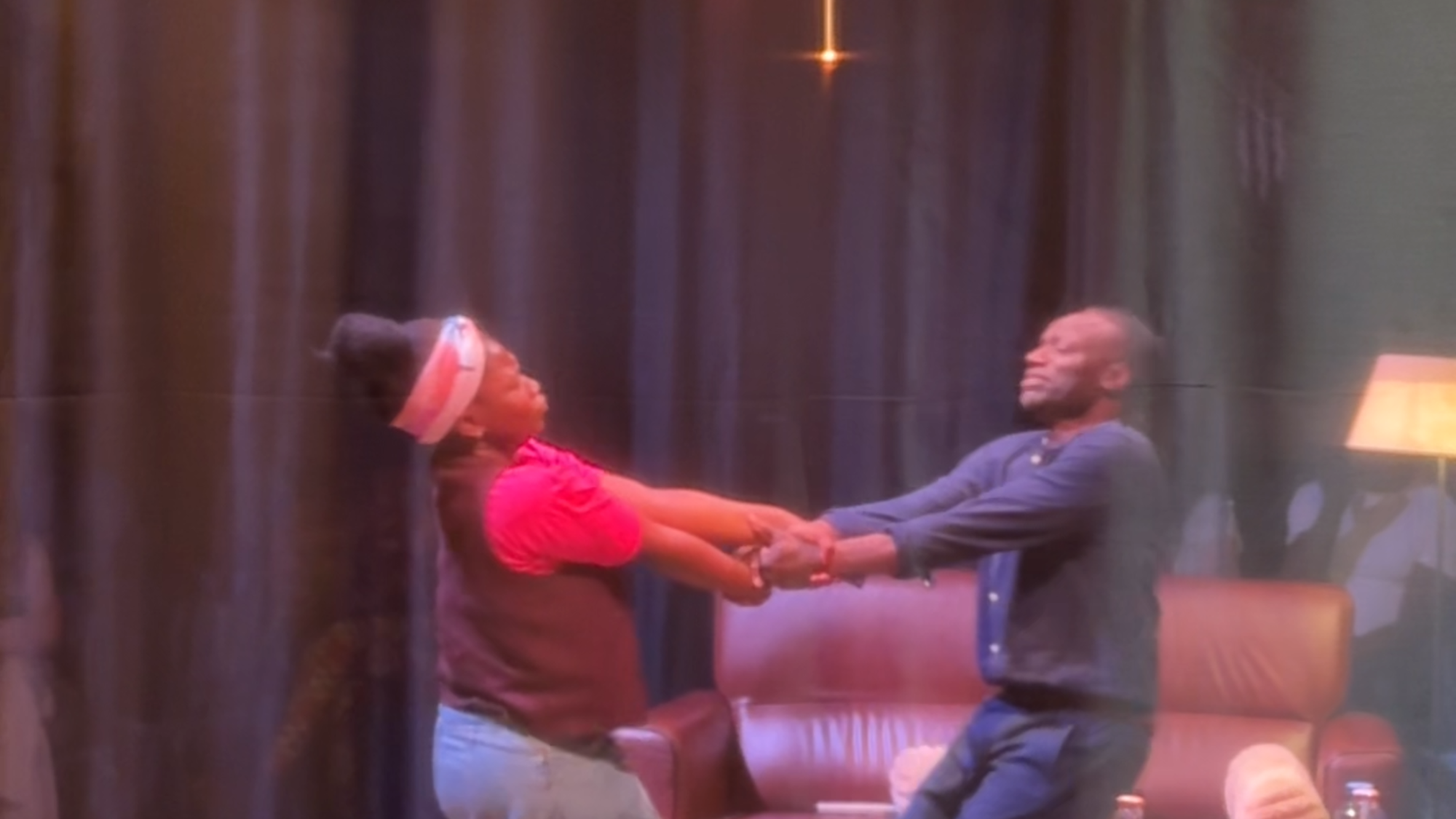 Op deze foto zien we de vader en dochter uit het toneelstuk dansend op het toneel. Er is een kleine woonkamer nagemaakt, met een tafel en stoelen en een bank met lamp ernaast.