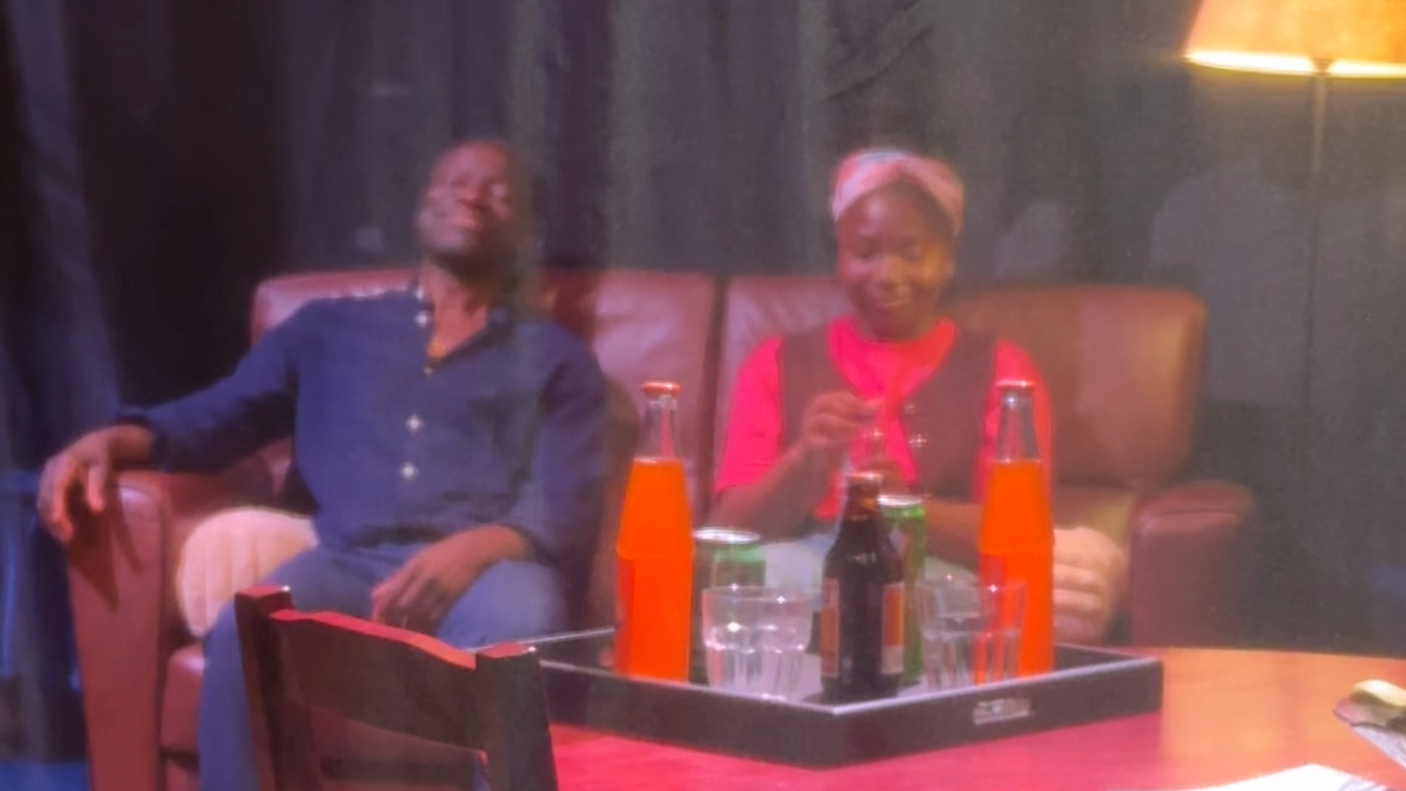 Op deze foto zien we de vader en dochter uit het theaterstuk op de bank op het toneel zitten. Er hangt een gaasdoek tussen ons en het podium in.