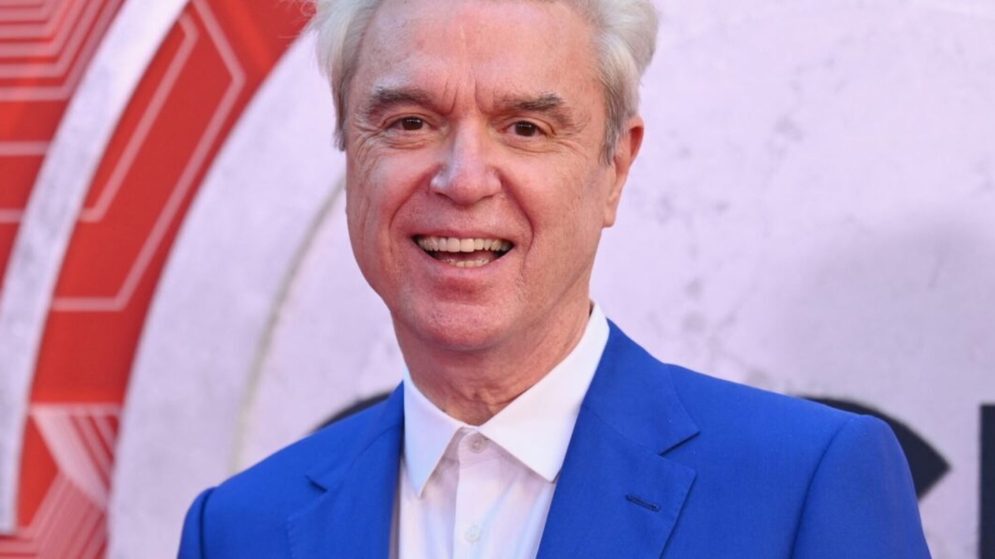 Zanger David Byrne staat lachend naar de camera in een blauw pak