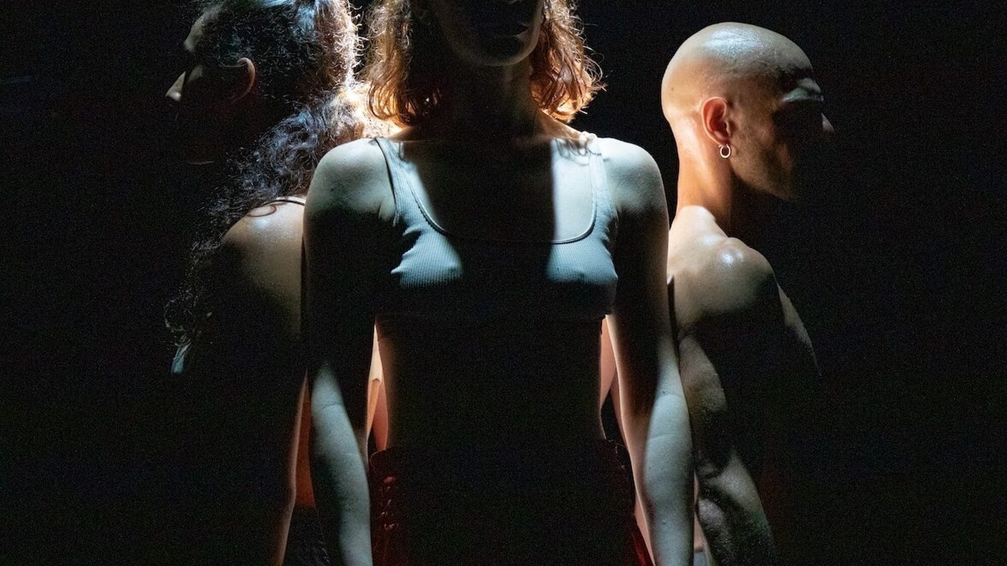 Drie dansers staan op een donker toneel.