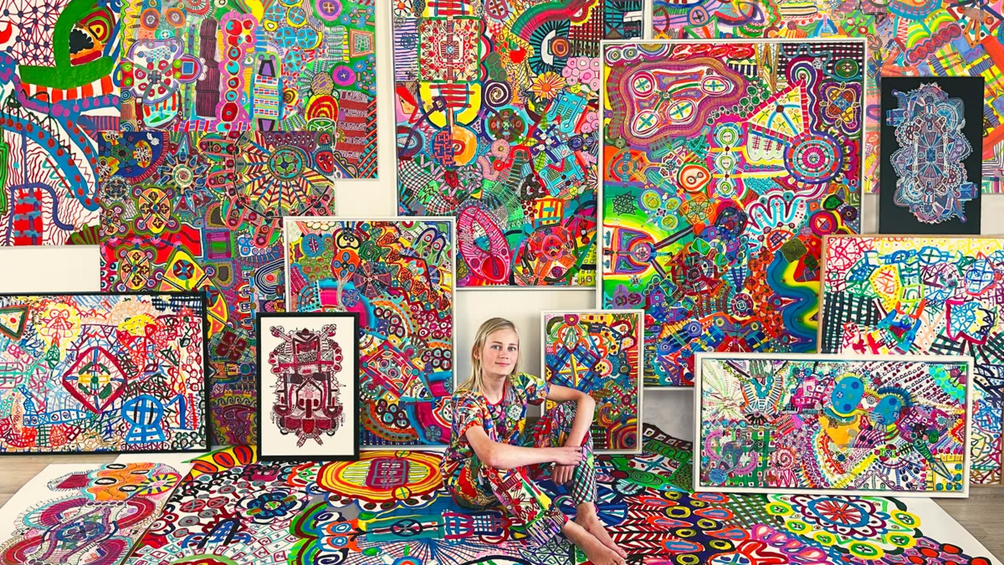 Jonge blonde jongen in een kleurijke outfit zittend tussen zijn kleurrijke lijnkunstwerken