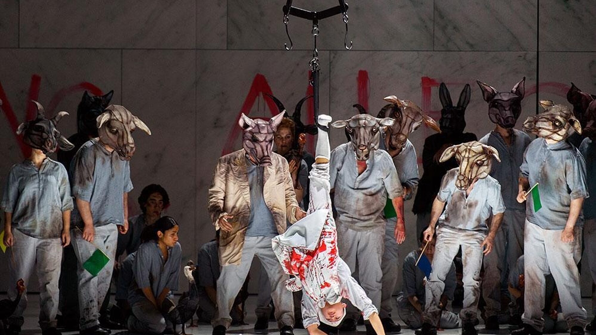 Hier is op een podium iemand te zien die een halve handstand doet. Eromheen staan meerdere mensen met een beestenmasker op hebben.