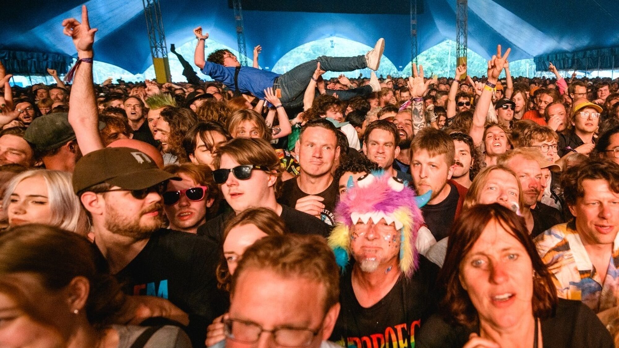 een foto van het publiek in een drukke tent. het is chaotisch en je ziet iemand crowdsurfen
