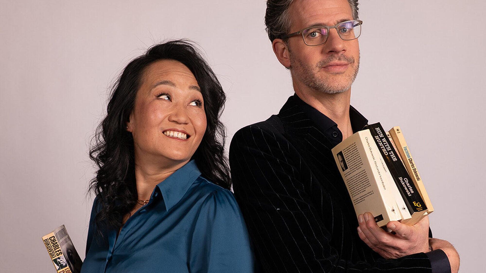 Een man en een vrouw staan naast elkaar met een boeken in de hand en de vrouw kijkt lachend naar de man