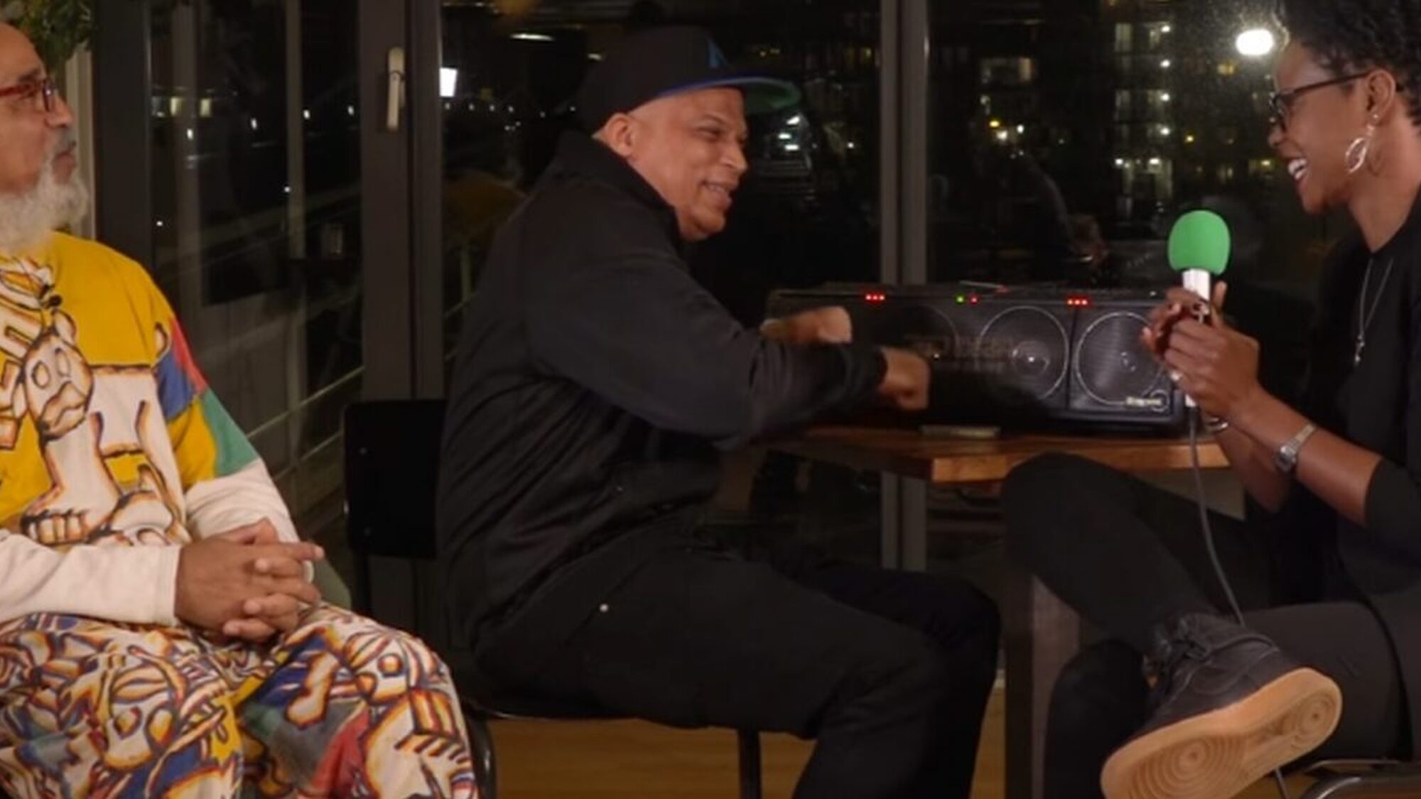 Drie mensen zitten lachend rond een tafel met een dj-set aan