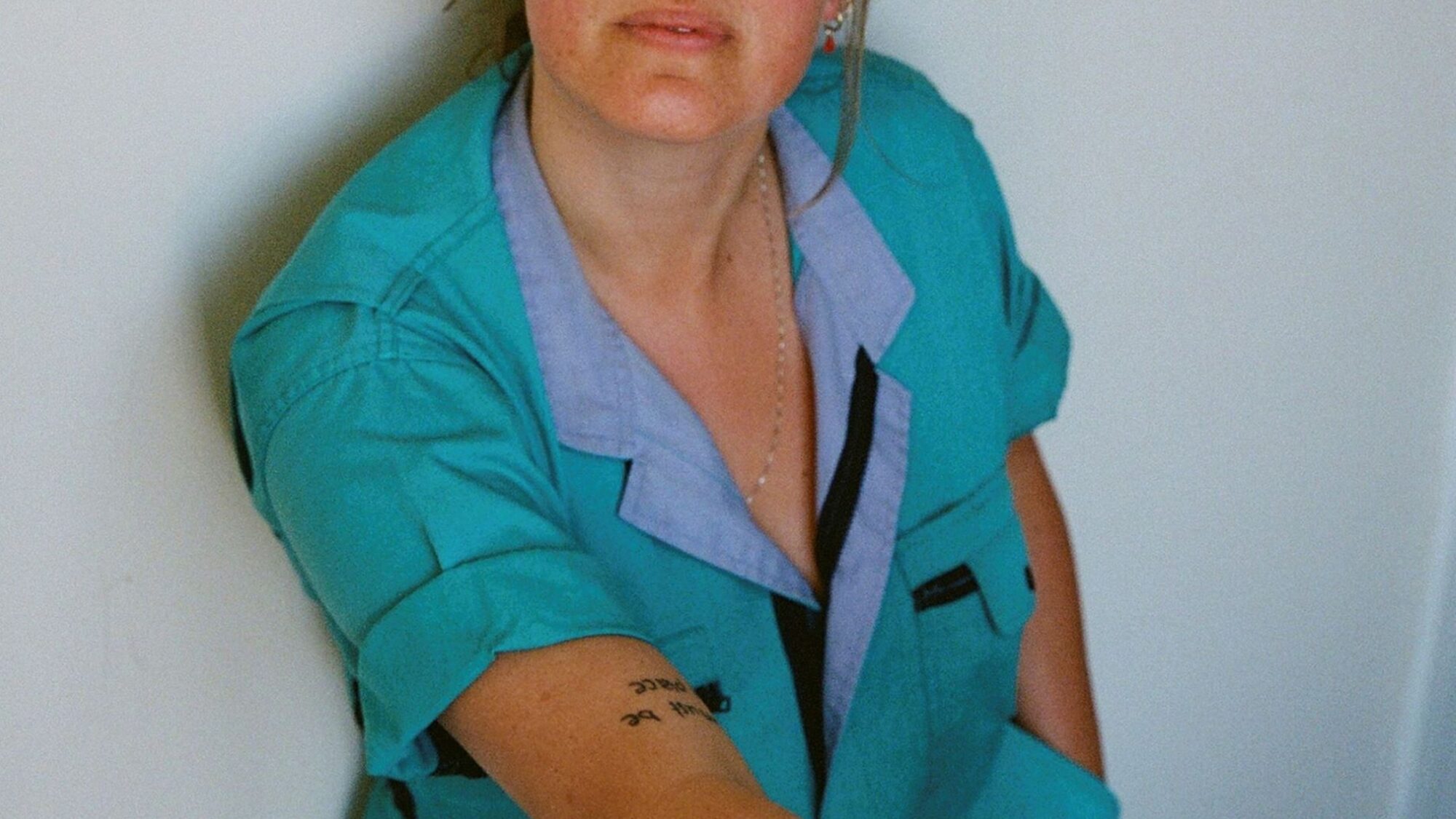 Actrice Laurien van Rijswijk staat tegen een witte muur. Ze draagt een blauwe overal en haar haar in een knot.