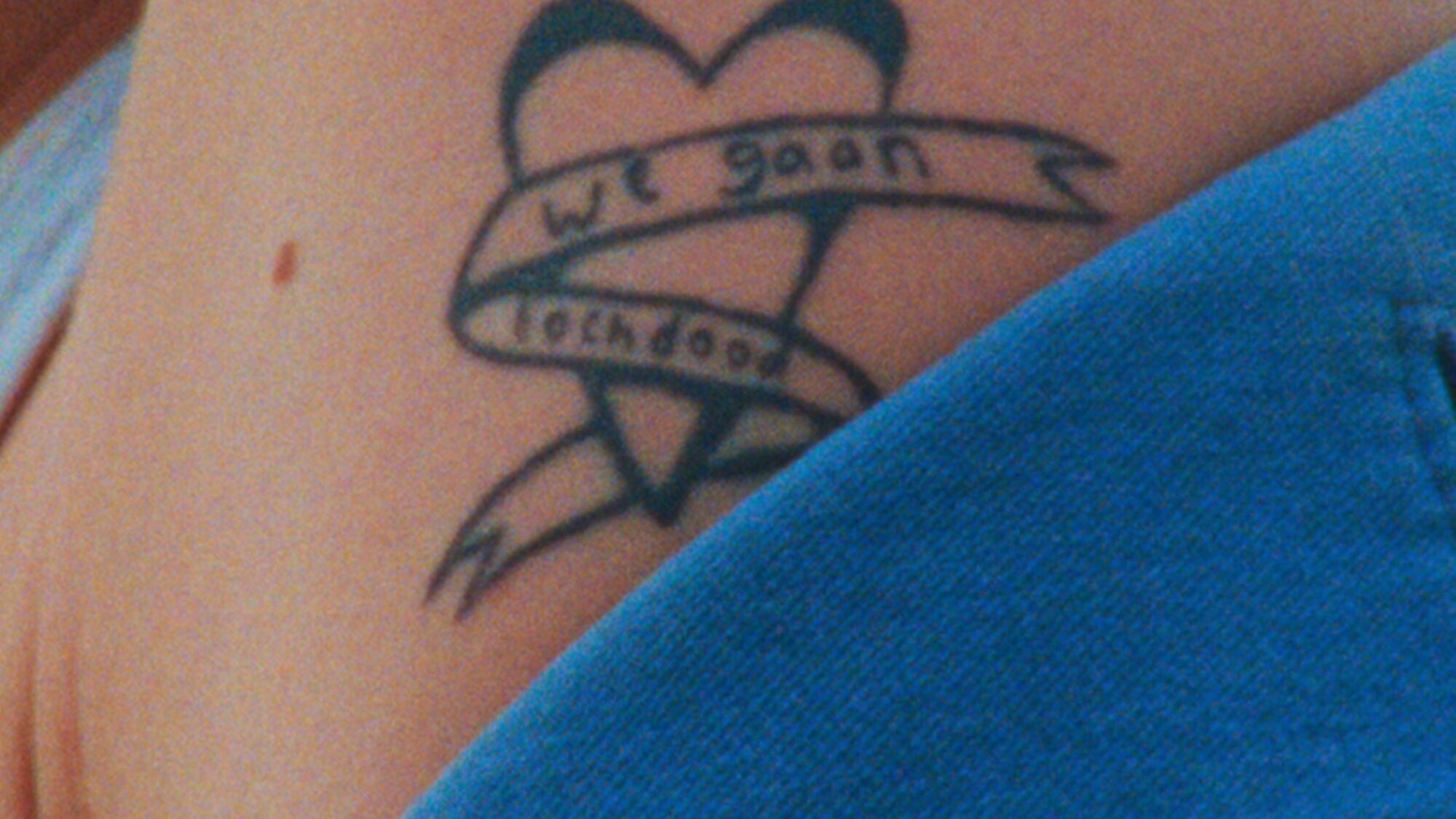 Blote schouder met tattoo. De tattoo is een hart met een lint eromheen, waarop staat 'We gaan toch dood'.