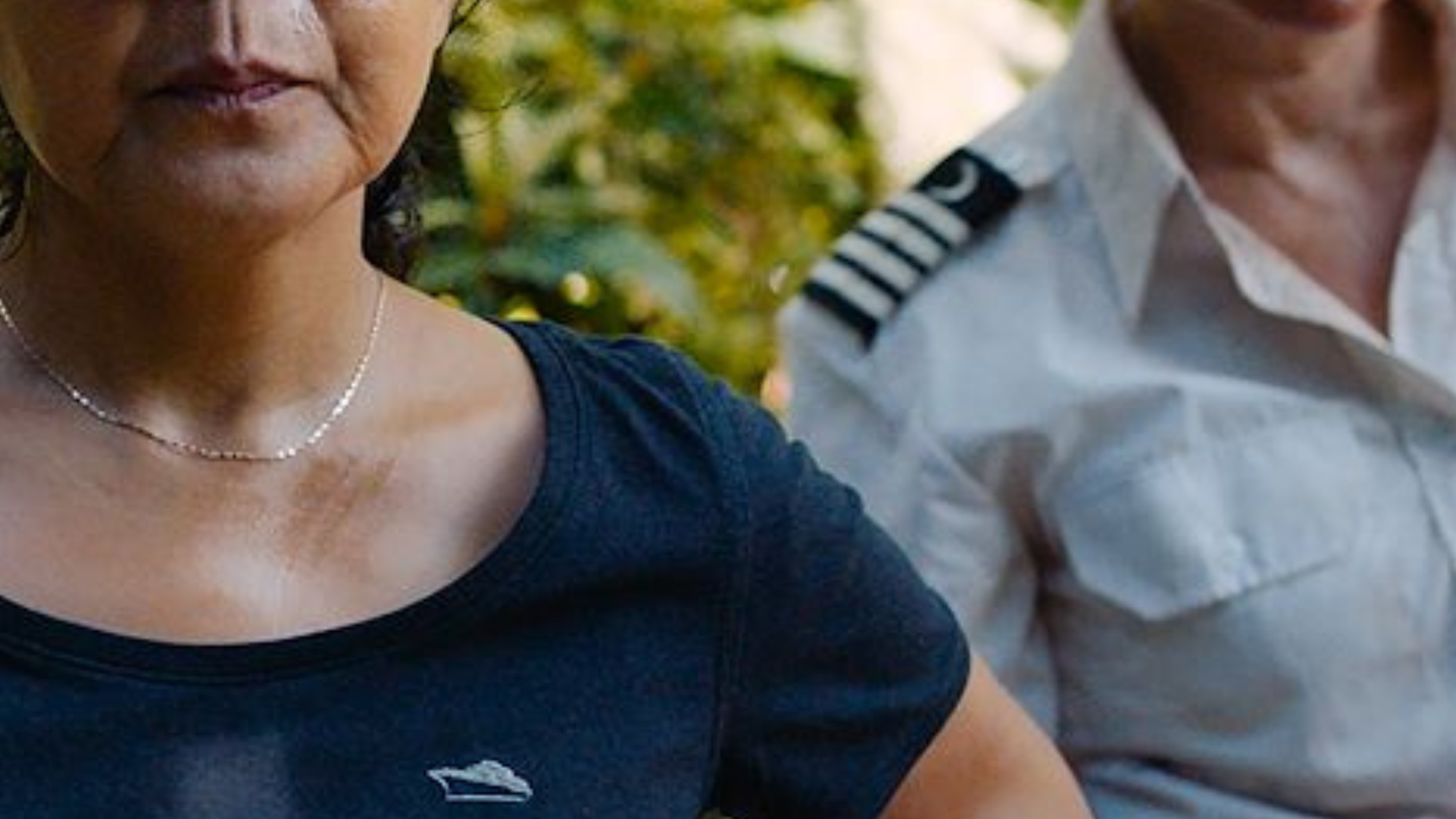 Er staan twee vrouwen op het beeld. De linker vrouw staat met haar handen in haar zij en heeft een zwart T-shirt aan en een zwarte pet op. De rechtervrouw heeft kort geblondeerd haar en heeft een kapiteinkostuum aan.