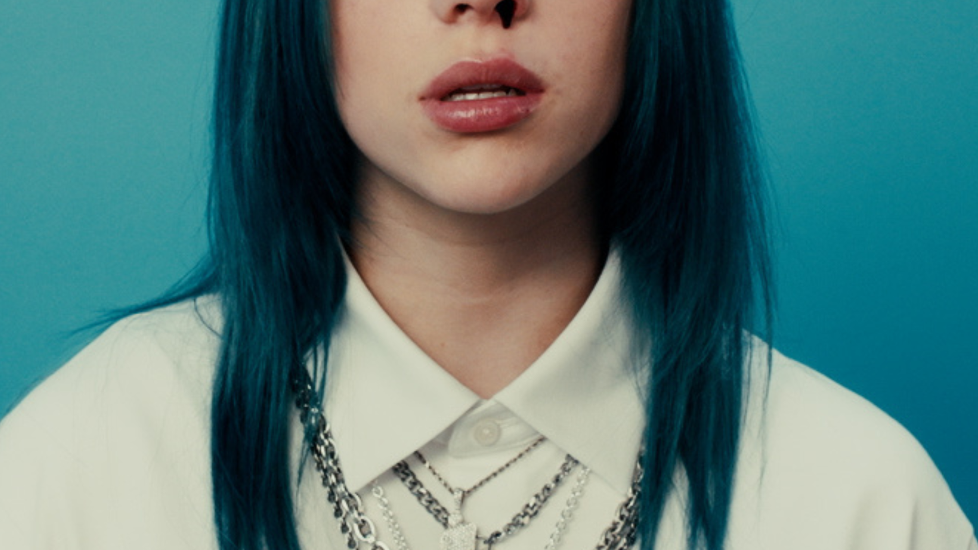 Zangeres Billie Eilish staat voor een blauwe muur. Ze heeft blauw haar, draagt een wit overhemd met kettingen erover en er komt bloed uit haar neus.
