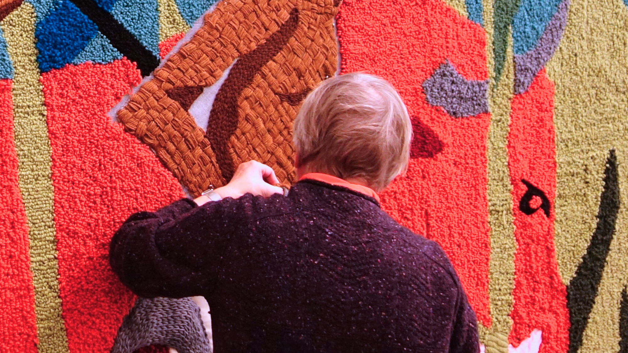 Er wordt door twee vrouwen gewerkt aan het wandtapijt. Op het tapijt staan twee personen, gebroken ketens, nootmuskaat en een palmboom.