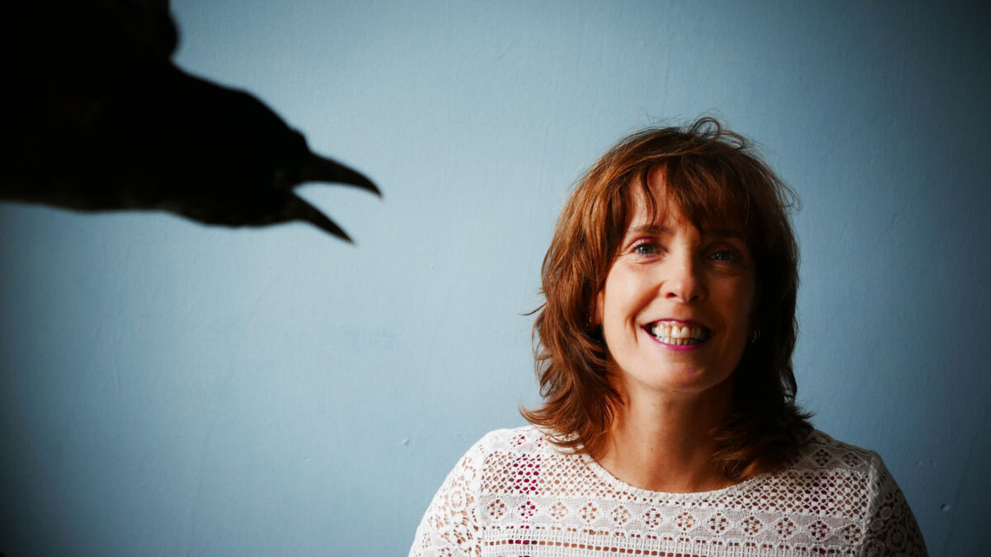 Schrijver Coco Schrijver lacht naar de camera, op links een schaduwfiguur van een kraai