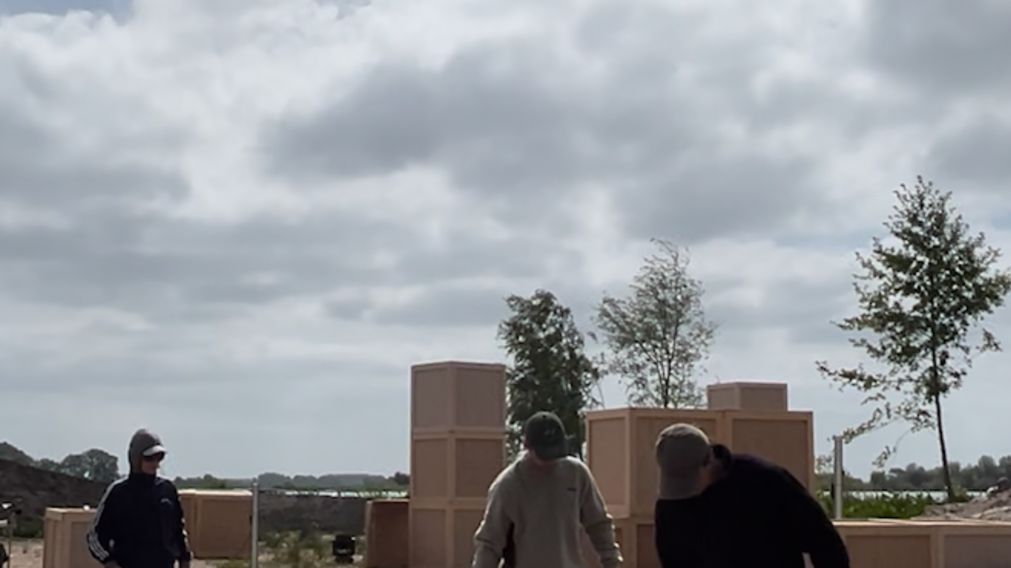Stil uit het stuk op locatie. De twee hoofdrolspelers gieten water uit een fluitketel op het zand van de zandafgraving.