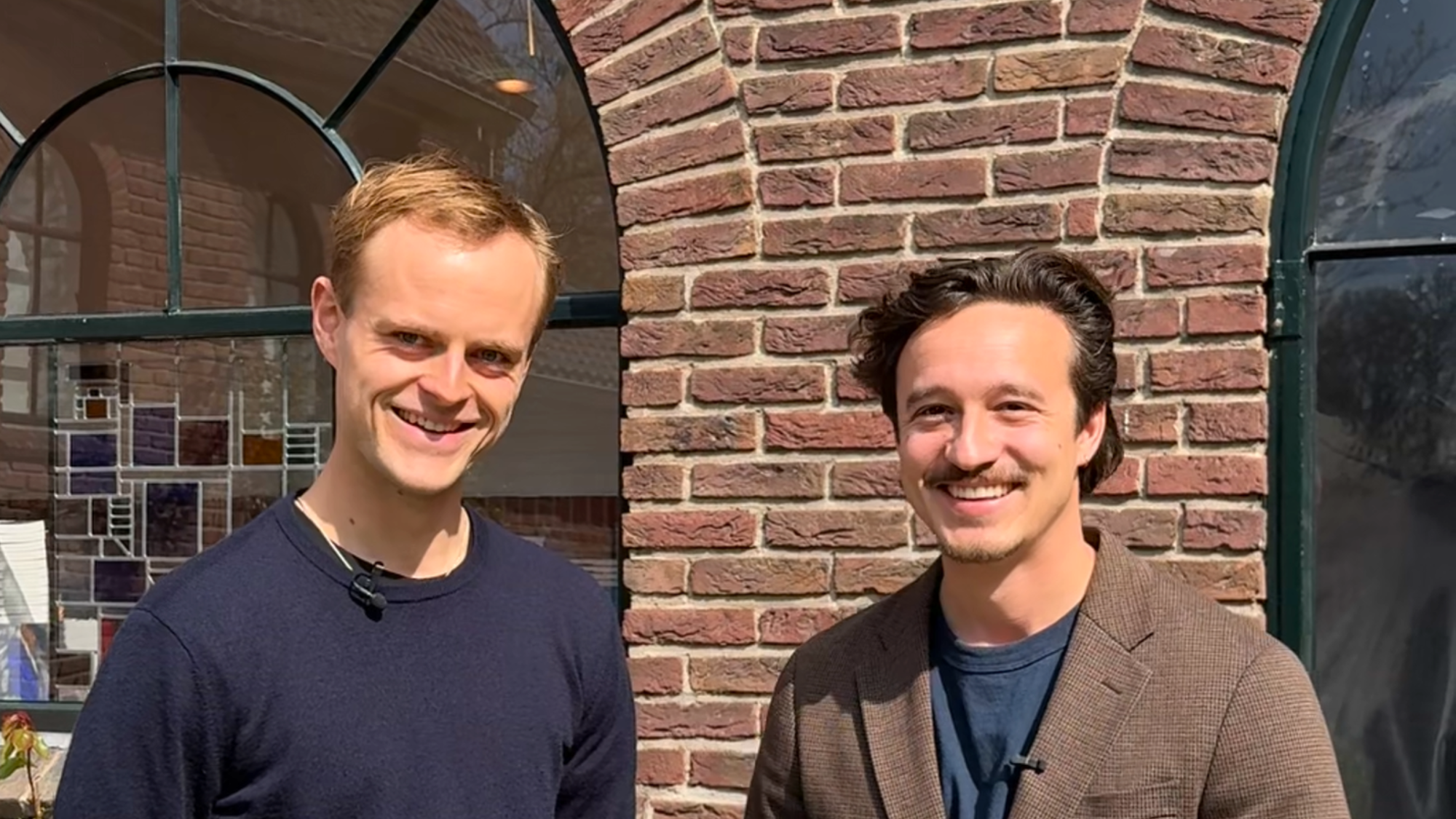 Foto van de twee hoofdrolspelers, Coen en Jurriaan. Ze staan voor een stenenmuur en kijken allebei vriendelijk de camera in.