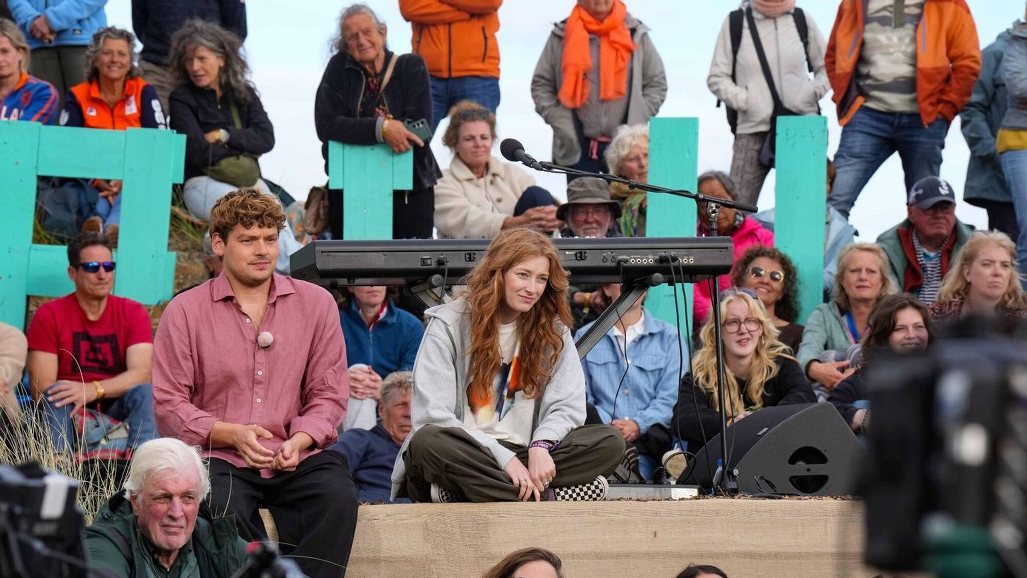 Veel mensen zitten in het gras of op het podium bij opnames van opium op oerol op terschelling