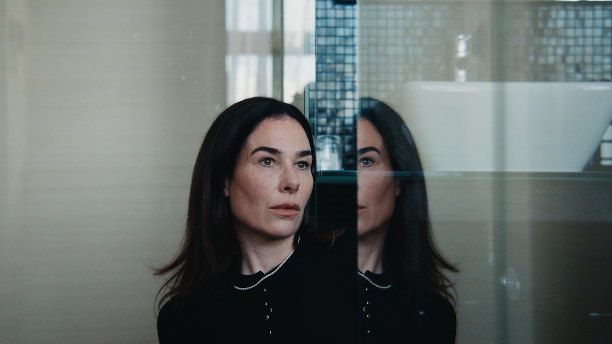 Vrouw met zwarte haren zit in de badkamer dromerig kijkend naar de camera