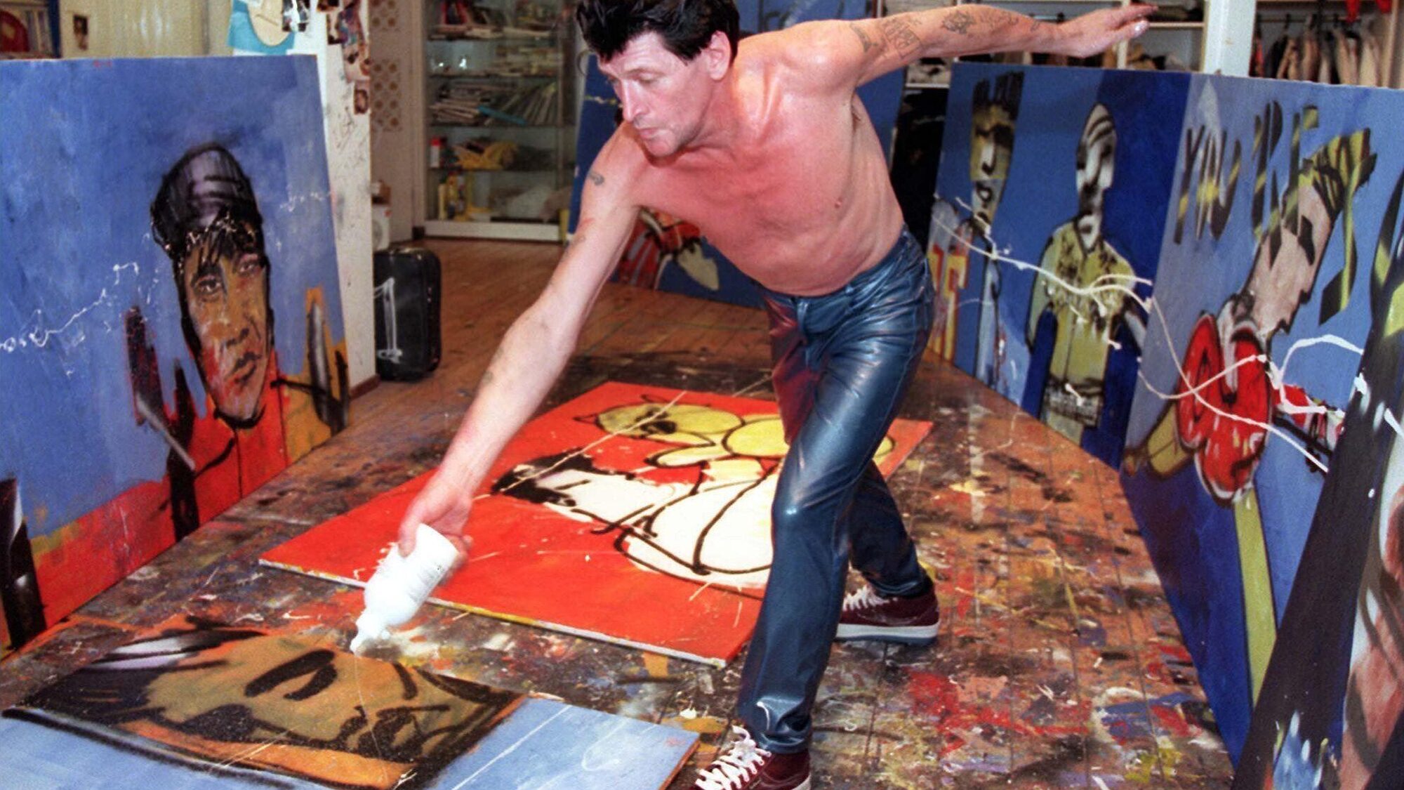 Herman Brood staat actief schilderend en spelend met zijn kunst in en atelier