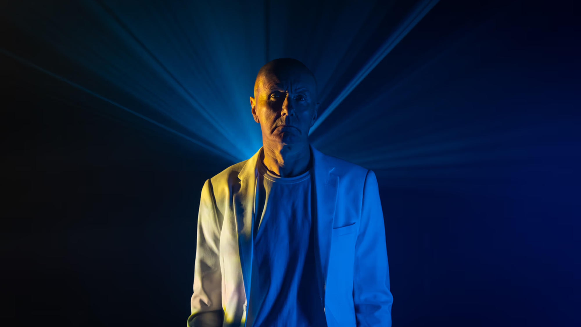 Man in wit pak staart mysterieus naar de camera met een blauwe laser achter zich
