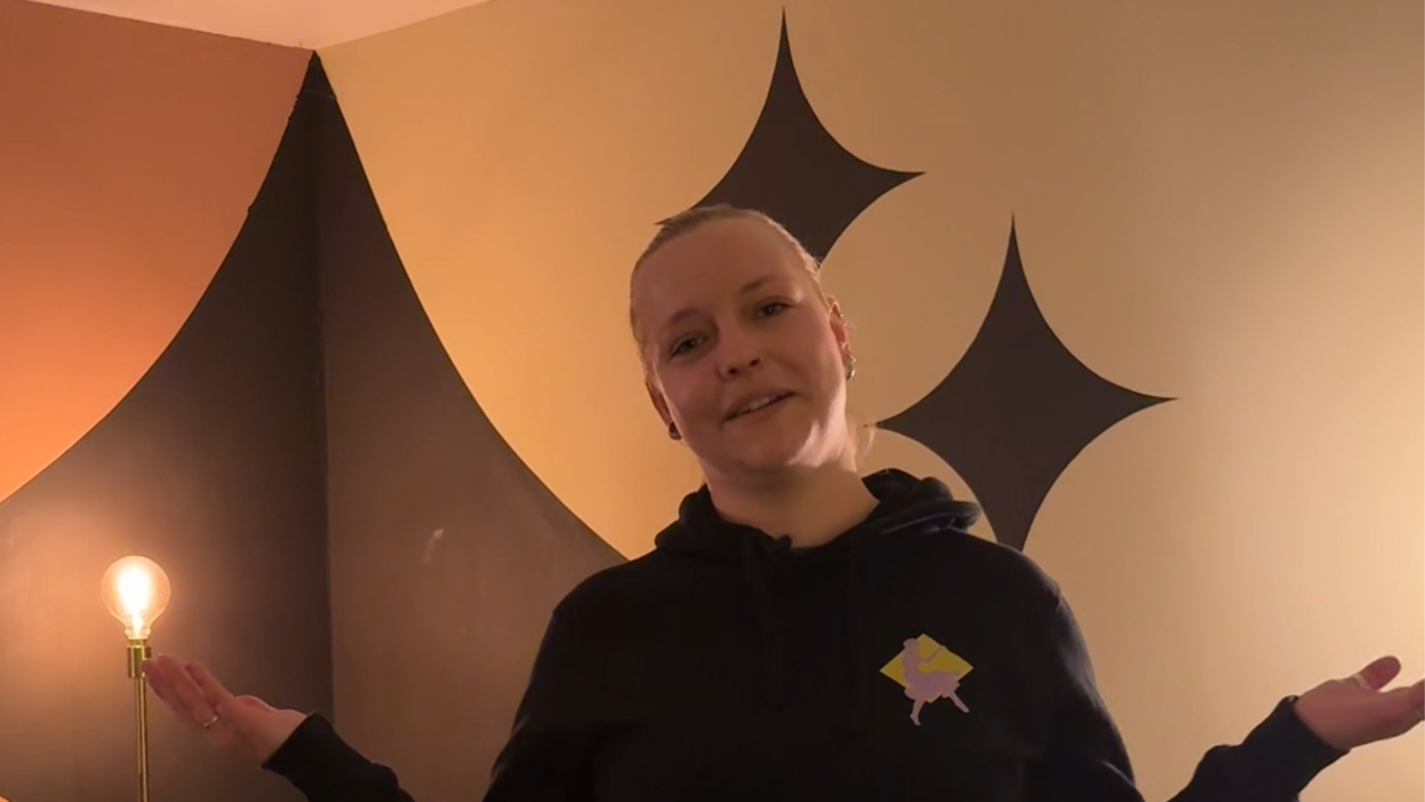 Izanka in de kleedkamer die ze laat zien. Ze houdt haar handen half omhoog naast haar lijf, alsof ze haar schouders ophaalt.