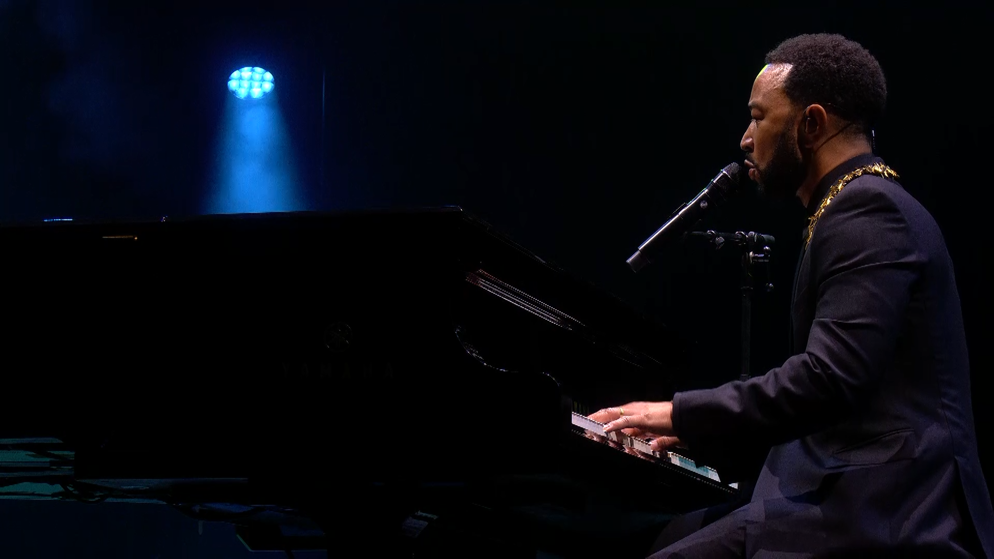 Zanger John Legend zit in een zwart pak achter zijn vleugel te zingen