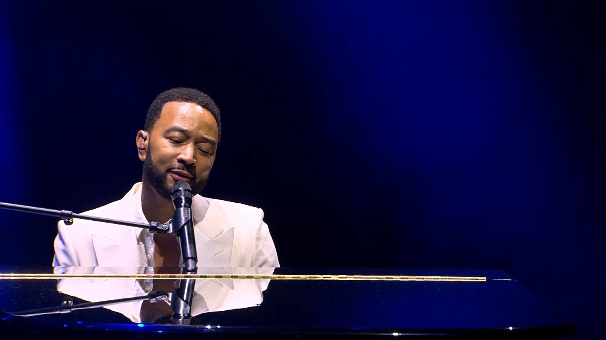 Zanger John Legend zit zingend achter zijn vleugel in een wit pak