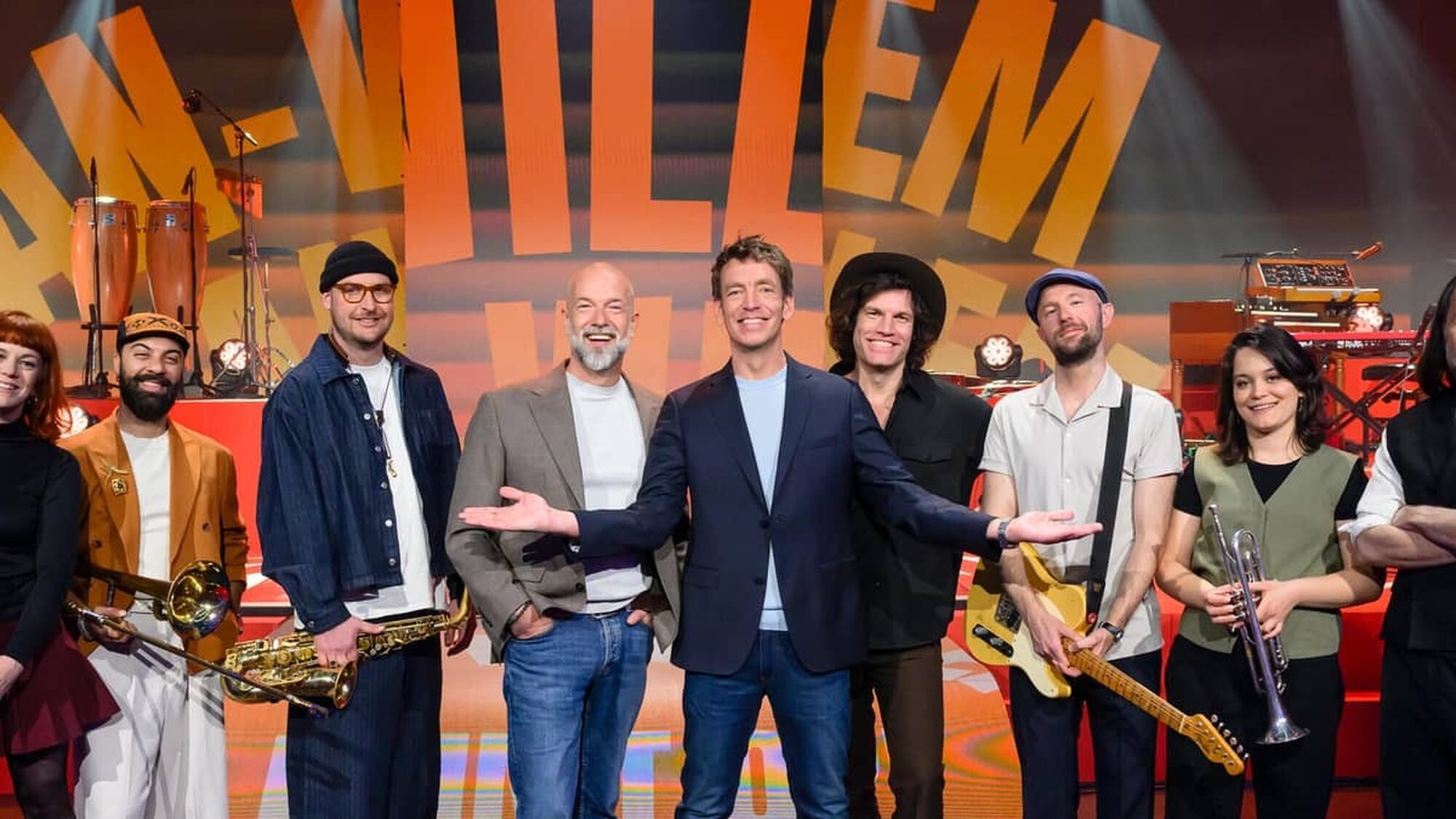 Veel mensen staan lachend in de studio met instrumenten vast