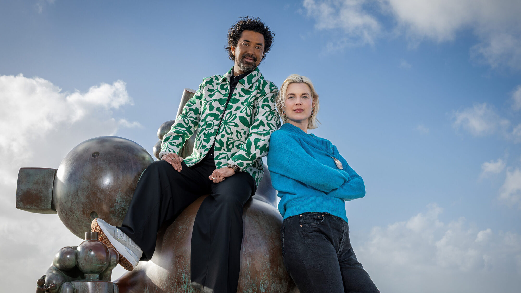 Man en vrouw poseren samen buiten op een kunstwerke kijkend naar de camera