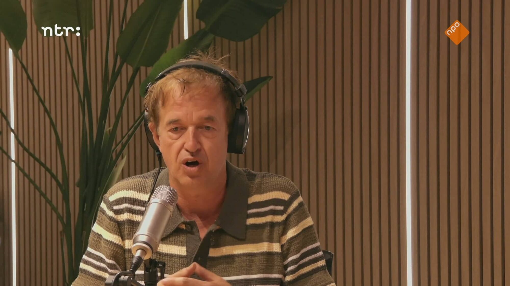 Man zit met een koptelefoon achter een microfoon te praten in een studio