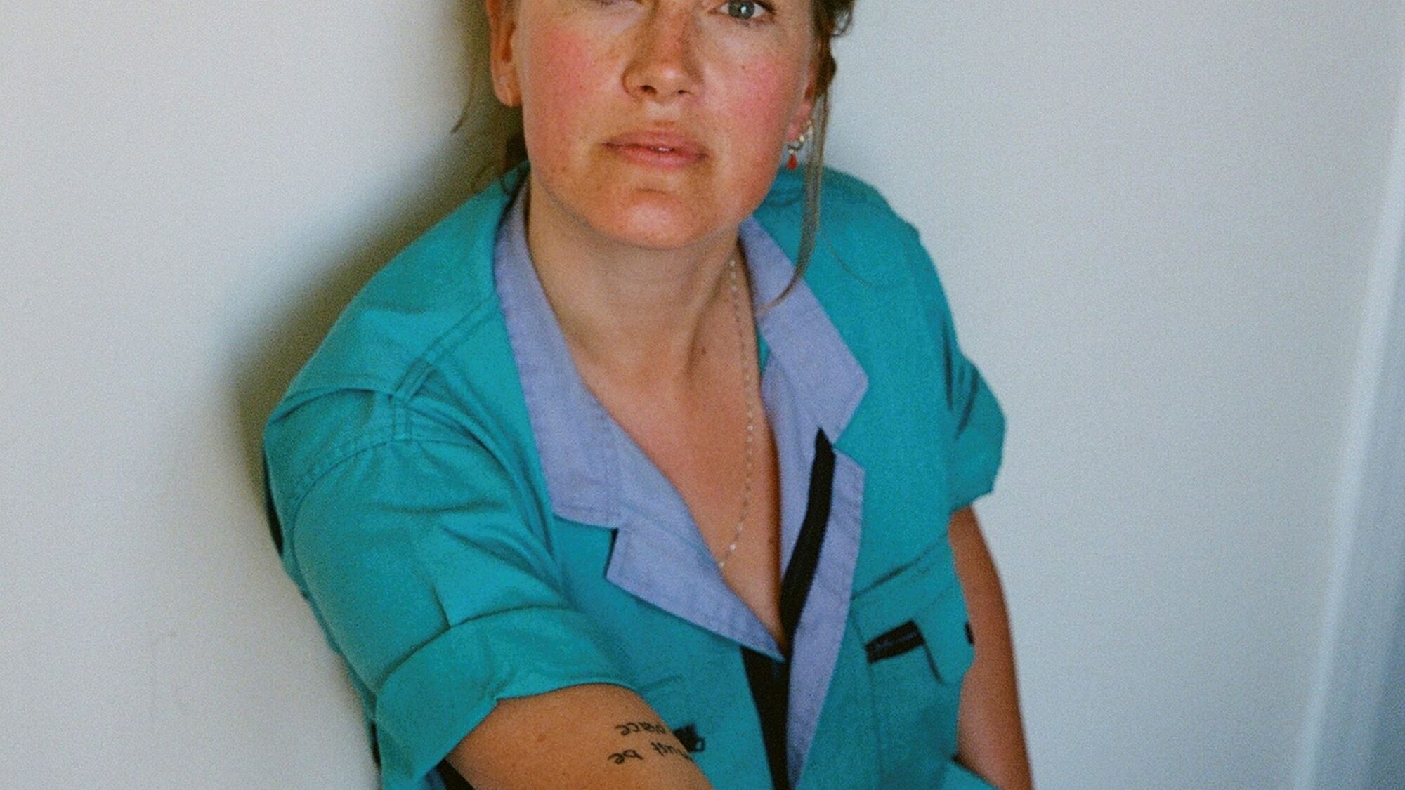 Actrice Laurien van Rijswijk staat tegen een witte muur. Ze draagt een blauwe overal en haar haar in een knot.