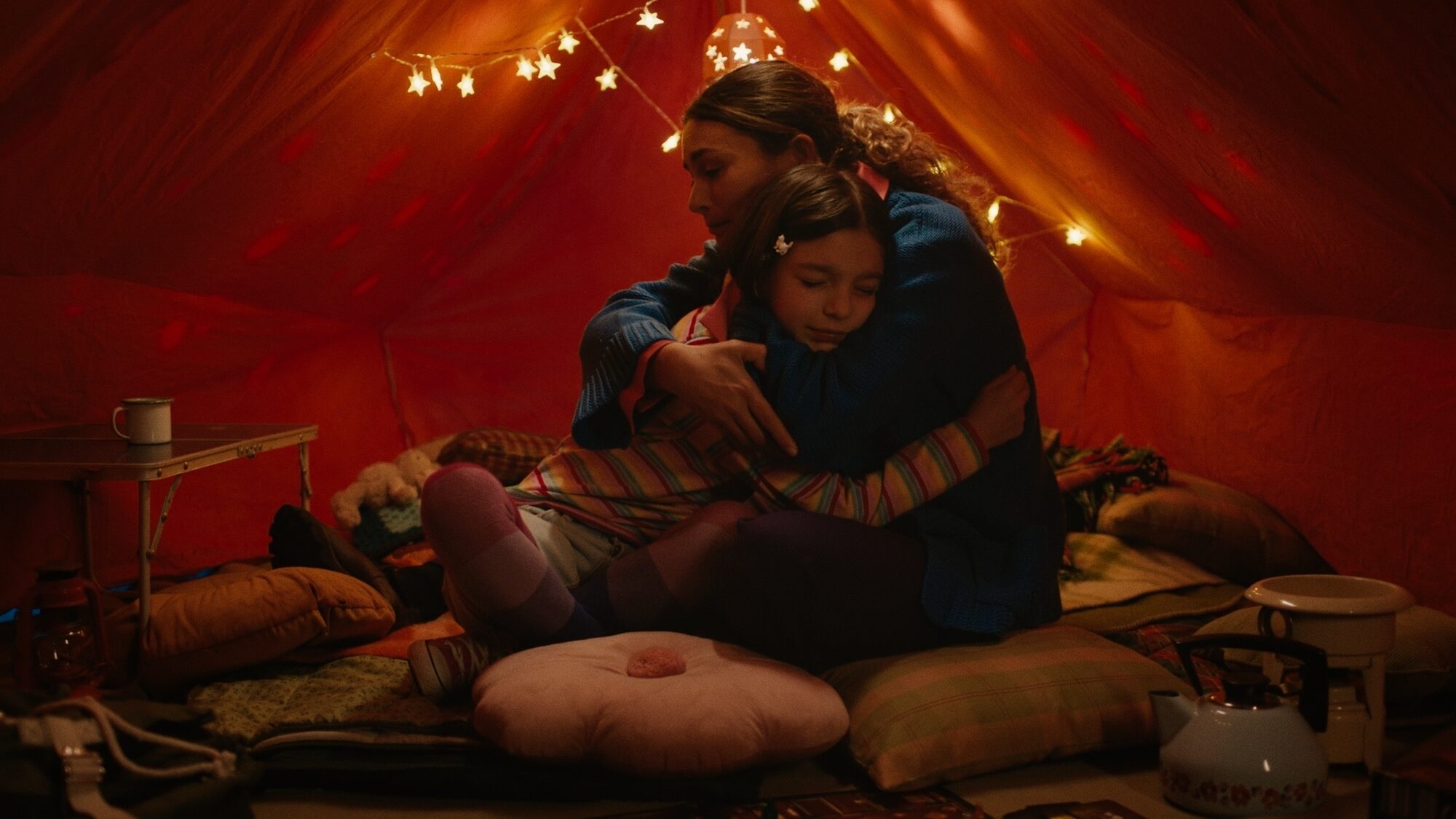 Je ziet een moeder en dochter in een tent met kerstlichtjes en kussens