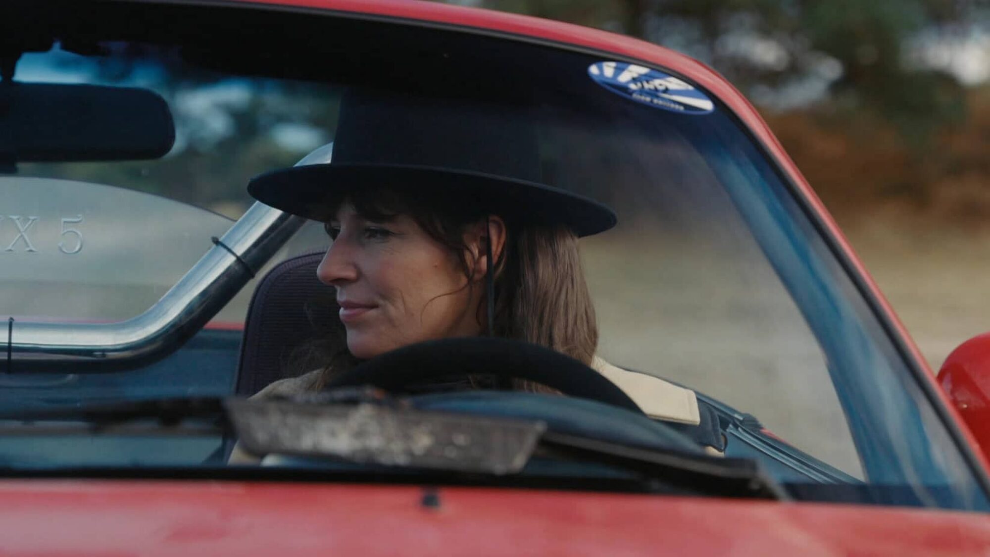 Vrouw met zwarte hoed zit in een rode auto