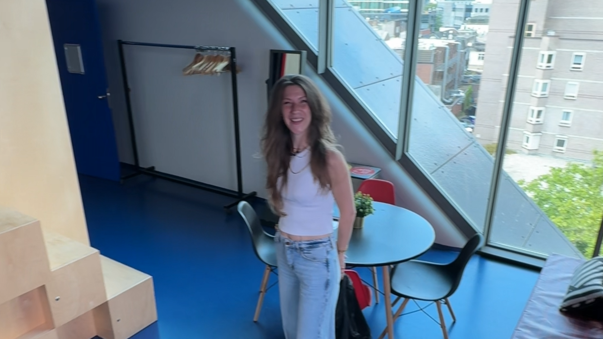 Foto van Nikki in de kleedkamer. Je ziet haar ten voeten uit in een kleedkamer met grote ramen en een blauwe vloer.