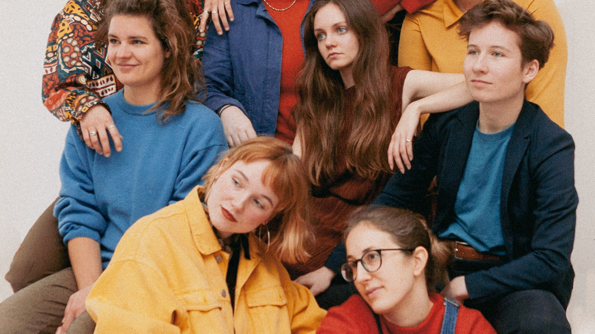 Dit is de persfoto van PARRA.DICE met de negen vrouwelijke/non-binaire bandleden. Ze zijn gekleed in het kleurpalette rood, blauw en geel.