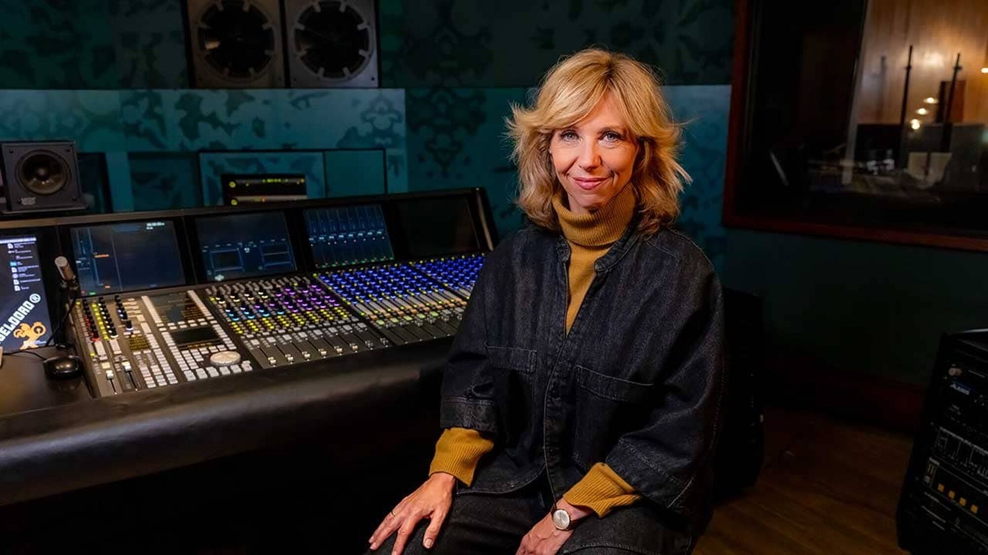 Zangeres Claudia de Breij in een muziekstudio kijkt lachend naar de camera