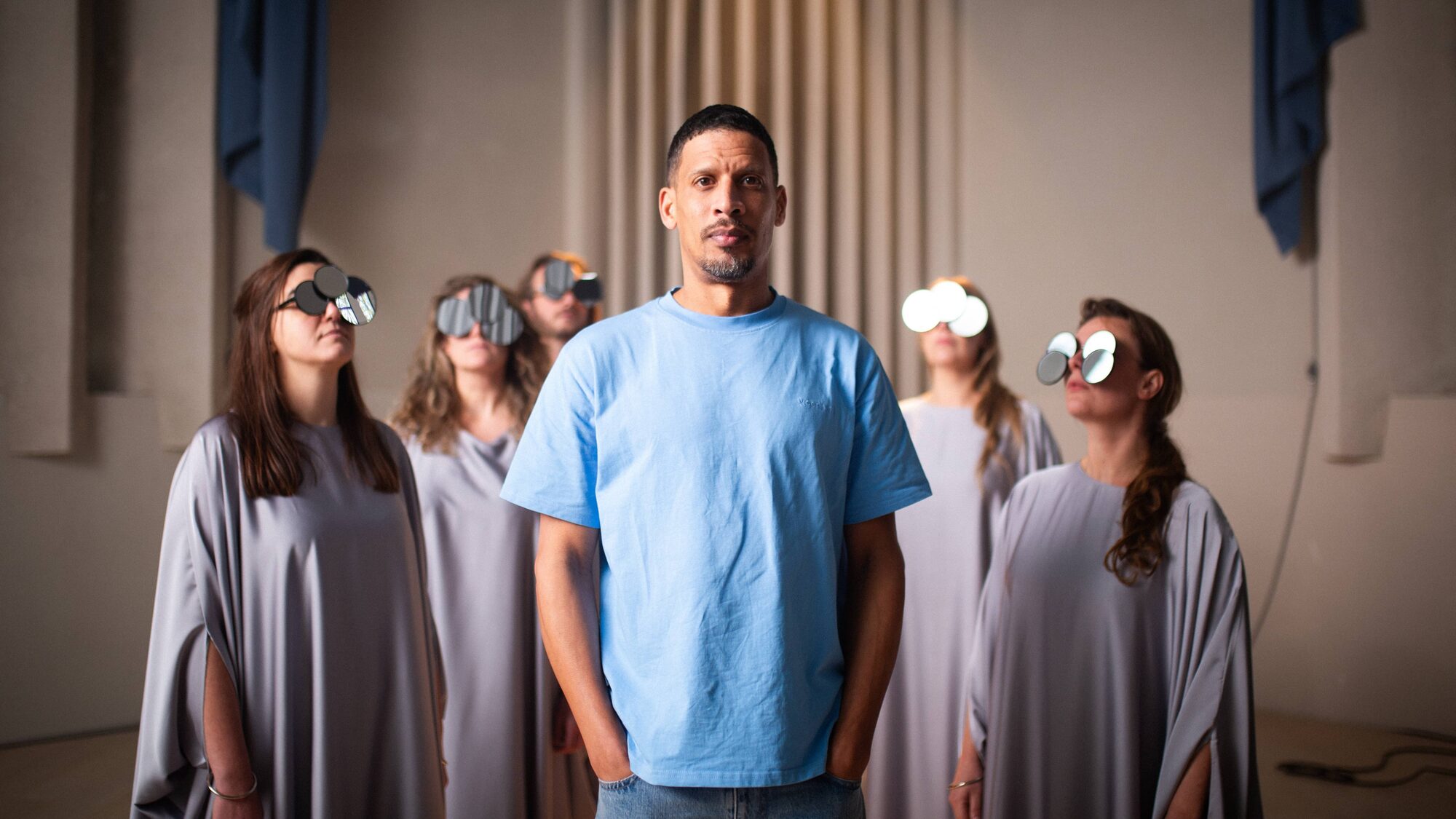 Man in blauw shirt staart dromerig richting de camera met mensen om zich heen bewegend