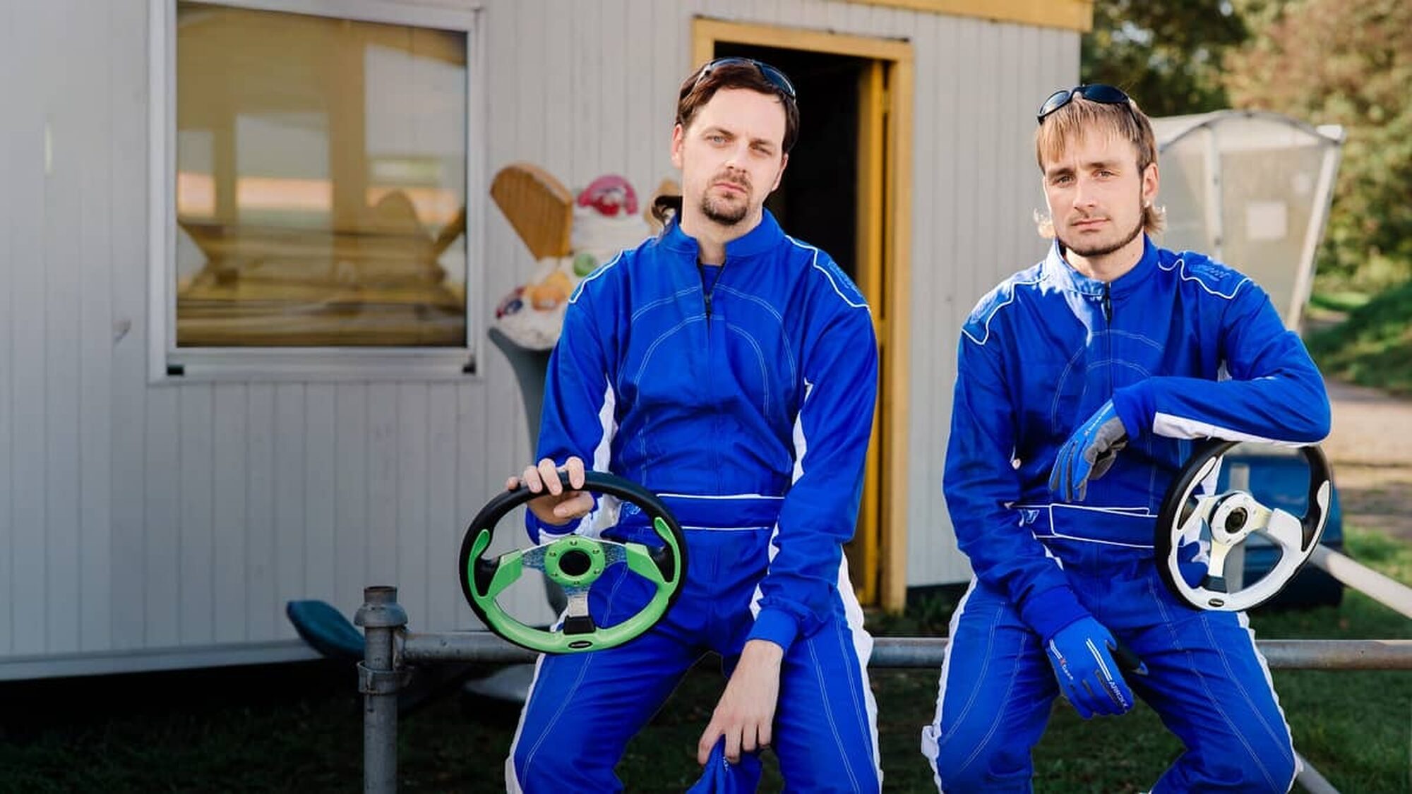 Twee witte mannen van Rundfunk zitten in een blauw pak op een tafel met een stuur in hun hand voor een containerhuisje.