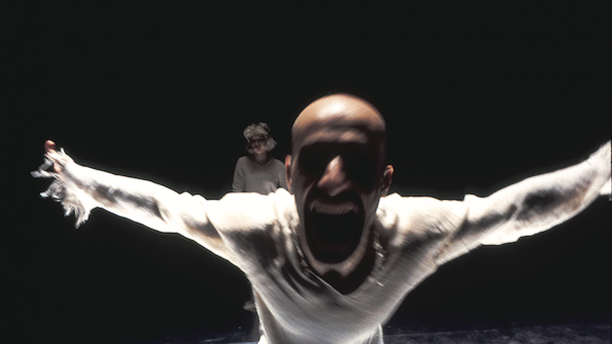 Danser schreeuwt en loopt met gespreide armen op de camera af.