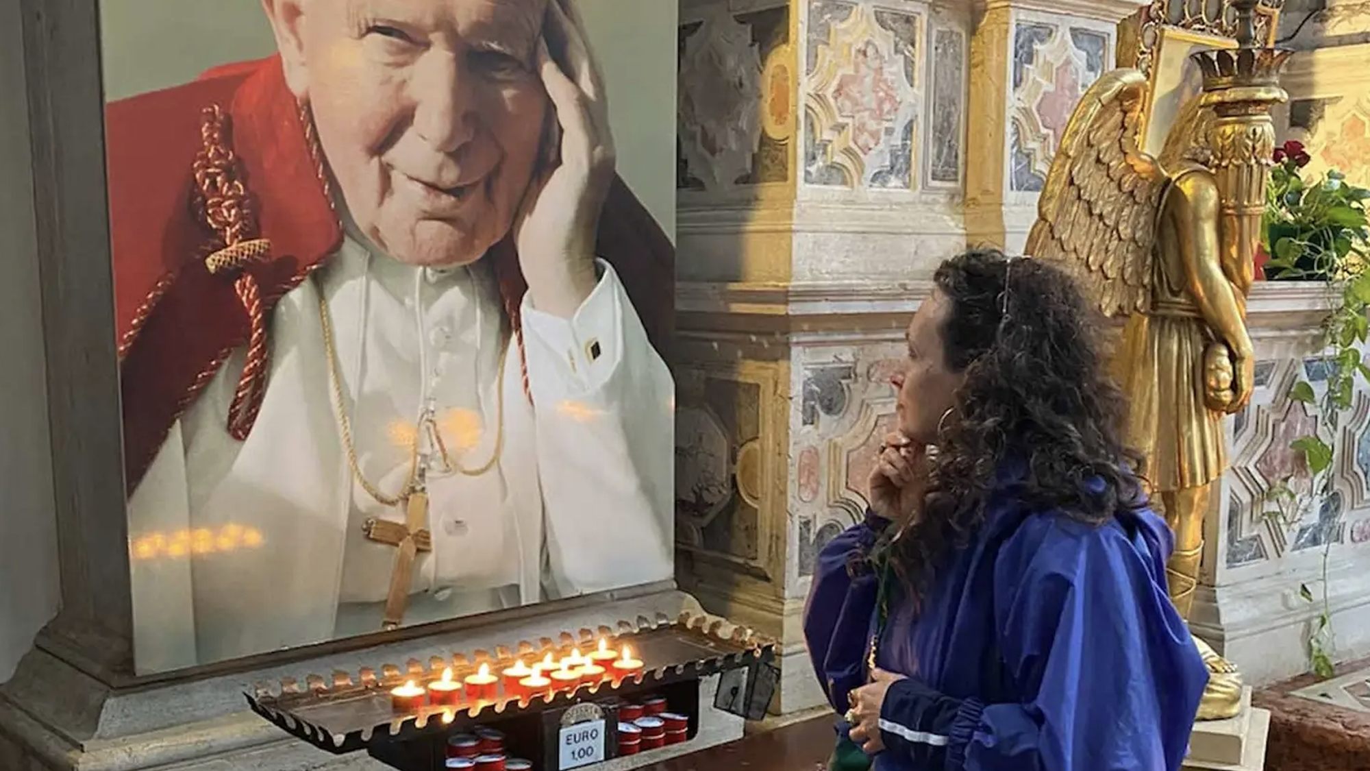 Olga Majeau kijkt naar een foto van de paus in een kerk waar kaarsjes zijn aangestoken