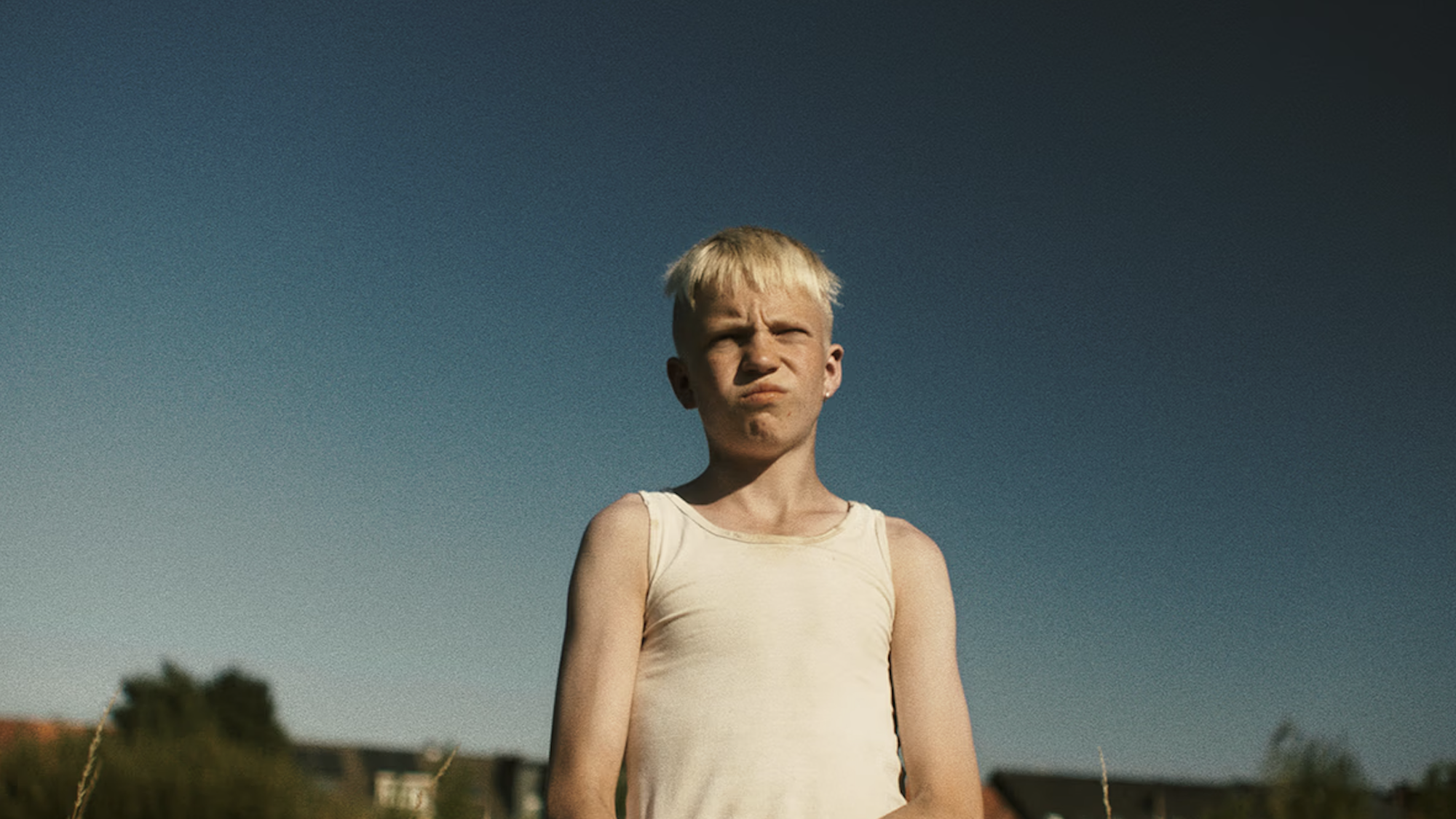 Jongen staat in een wit hemd voor een rijtje huizen