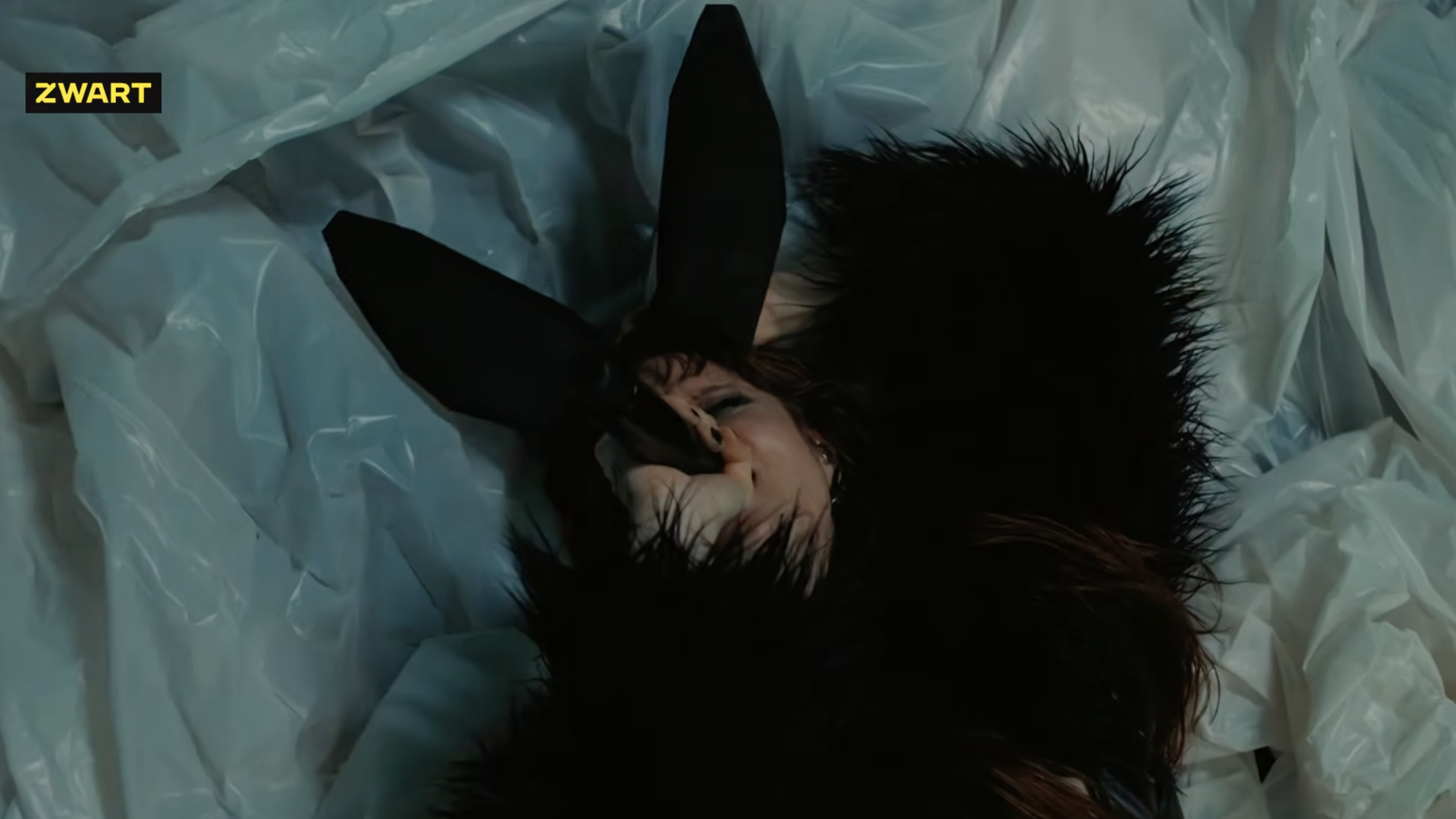 Zangeres MEROL ligt op een plastic zeil in een zwart harige outfit en konijnenoren op