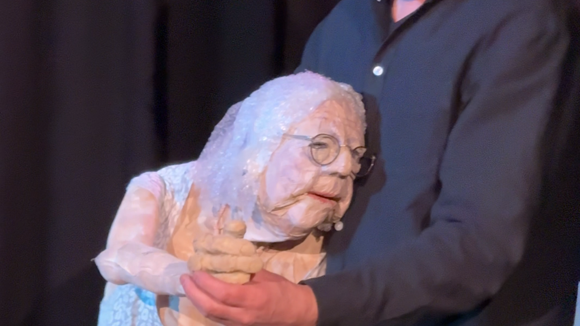 Een foto van Servaes de poppenspeler met zijn moeder. Ze staan en dansen, de pop is een stuk kleiner dan Servaes. Servaes kijkt lachend naar beneden.