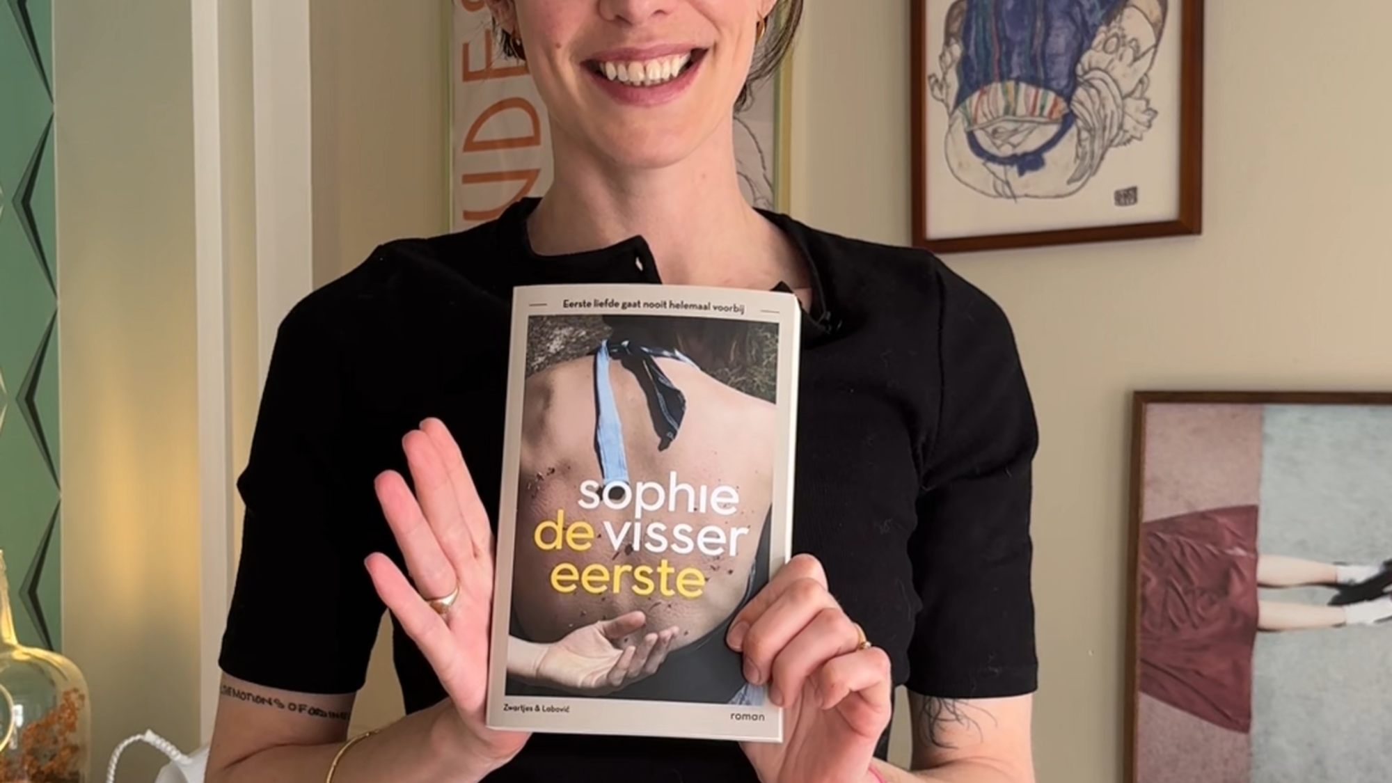 Schrijfster Sophie Visser staat met haar boek in haar handen. Ze laat het lachend aan de camera zien.
